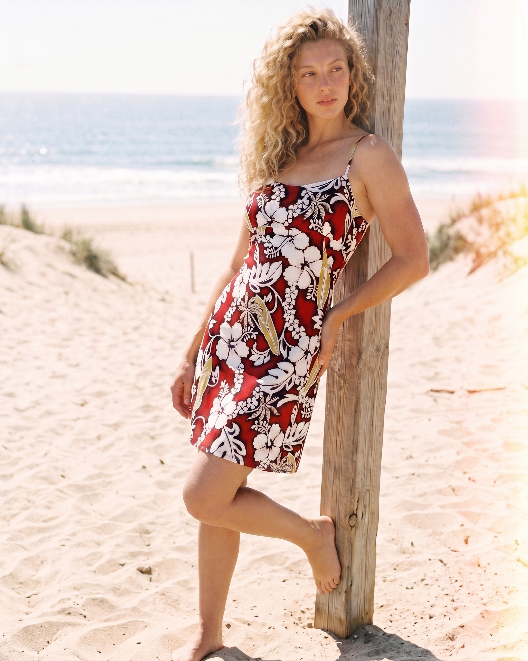 Short-Spaghetti-Strap-sundress-Hang-Loose-Red-Model-on-the-beach-leaning-on-a-beach-pole-full-body-shot